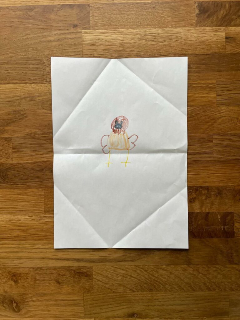 Auf dem Papier ist eine kindliche Zeichnung eines Vogels mit bunten Federn und gelben Beinen, rote Flügel, Orangen Körper und Roten Kopf mit einem Schwarzen Schnabel zu sehen.